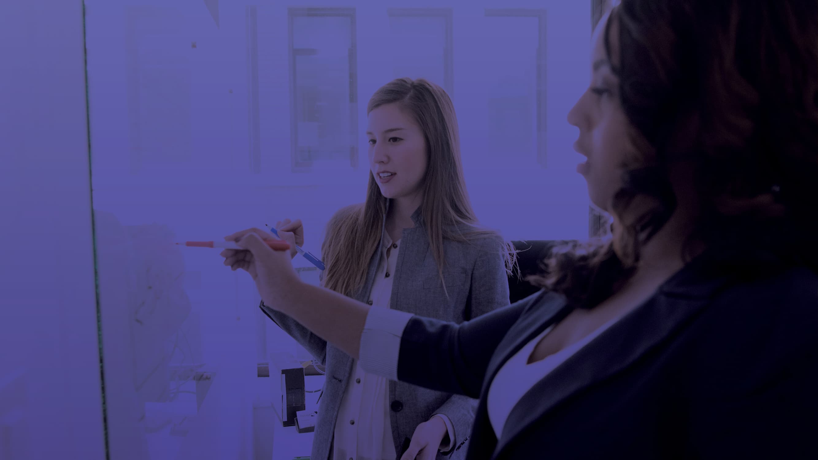 Two women looking at trends on a white board