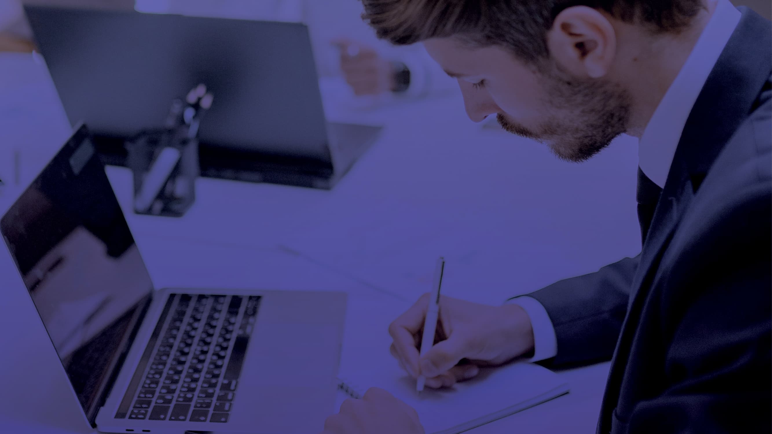 Man with laptop writing on a piece of paper