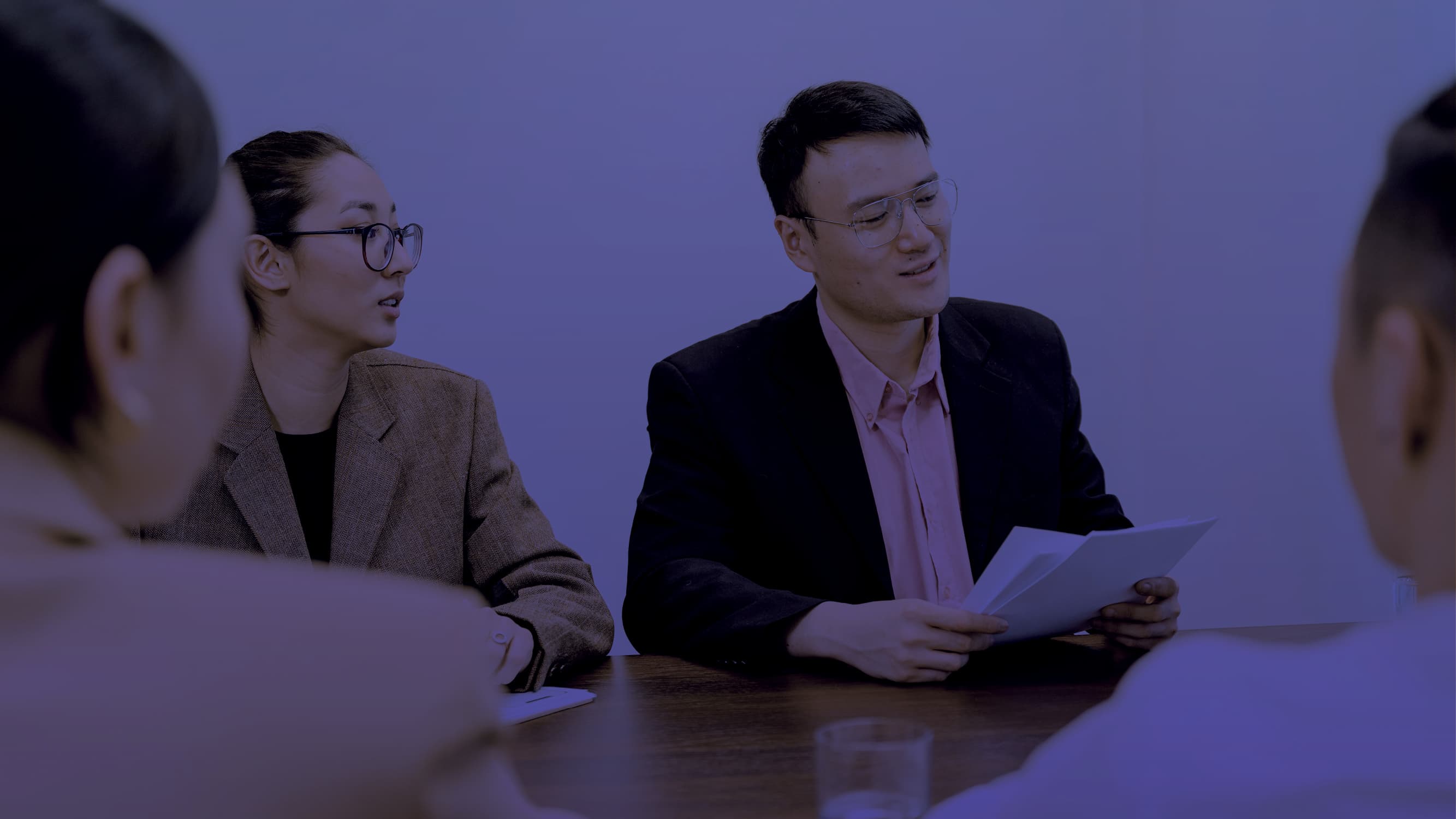 Businessman and woman sitting at a table with 2 clients discussing paperwork
